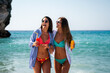 © NDABCREATIVITY - Two happy women toasting colorful beach drinks under the sun, enjoying tropical vibes and friendship