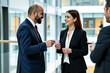 © Alex & M Studio - Professional business people in formal navy suits having conversation and exchanging business card in bright modern corporate office building with glass windows background