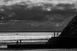 © Philip - Dramatic black and white coastal scene with silhouetted people standing on a harbour wall against a shimmering sea and dark storm clouds