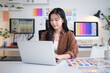 © wattana - emale designer working on a laptop, surrounded by vibrant color charts and palette references in a modern creative studio.