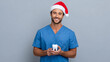 © Yulia - Portrait of young male dentist in Santa hat with tooth on light blue background