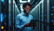 © miss irine - African American engineer uses tablet in server room. Modern data center with information storage, digital network. Man works with wireless mobile tech in electronic science, global business