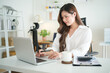 © wattana - Professional woman typing on laptop at modern white desk with coffee.