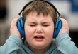 © Autism in Focus - Autistic child boy in noisy public space with blue noise cancelling headphones eyes closed showing hypersensitivity and frustration due to sound and sensory overload