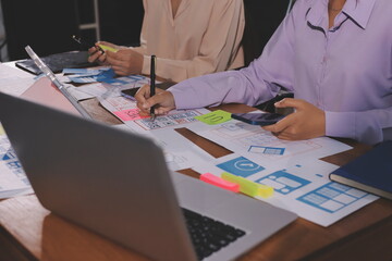 Close up ux developer and ui designer brainstorming about mobile app interface wireframe design on table with customer breif and color code at modern office.Creative digital development agency.