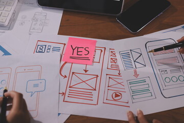 Close up ux developer and ui designer brainstorming about mobile app interface wireframe design on table with customer breif and color code at modern office.Creative digital development agency.