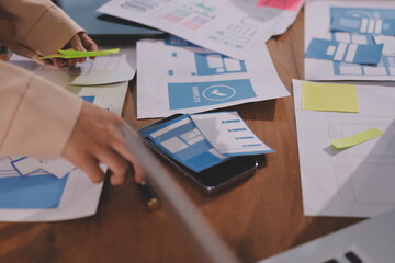 Close up ux developer and ui designer brainstorming about mobile app interface wireframe design on table with customer breif and color code at modern office.Creative digital development agency.