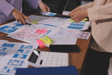 Close up ux developer and ui designer brainstorming about mobile app interface wireframe design on table with customer breif and color code at modern office.Creative digital development agency.