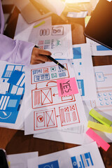 Close up ux developer and ui designer brainstorming about mobile app interface wireframe design on table with customer breif and color code at modern office.Creative digital development agency.