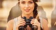 © Liza - Young woman holding binoculars and looking forward outdoors