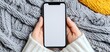 © imagineRbc - Woman holds a mobile phone with a blank screen over a warm, knitted grey blanket