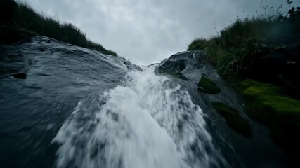 Wall Mural - A tracking shot follows a stream of rainwater flowing rapidly down a natural rock formation, highlighting the power of nature under stormy skies commercial, outdoor, background