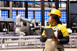 © DC Studio - Female industrial engineer walking through power plant with tablet in hand, overseeing machinery development. African American maintenance manager monitors production lines in manufacturing facility.