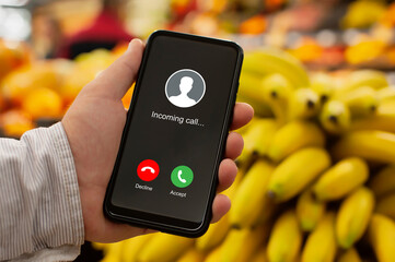 Modern smartphone displaying a generic incoming call screen with Decline and Accept buttons. The vibrant, blurred background of yellow bananas and other produce in a grocery store or market.