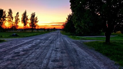 Wall Mural - Wide Gravel Road Leading Into Distant Horizon Under Glowing Summer Sunset Sky