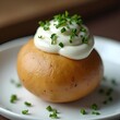 © Coffee_Reflections - Round orange baked potato topped with white cream sauce and garnished with fresh green herbs, elegantly presented on a white plate