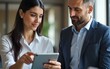 © Susan - A woman points at a tablet screen while talking to a man, discussing information on the device in a professional setting. High quality