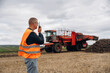 © standret - Conversation by walkie talkie. Farmer is working in the agricultural field. Against beet harvester