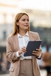 © Zoran Jesic - Businesswoman using digital tablet, walking in city, looking away