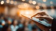 © Justlight - Closeup of a hand using a touchscreen device during a lively conference with blurred participants in the background emphasizing interactive engagement.