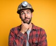 © free - A thoughtful man in a red and black checkered shirt, wearing a miner's helmet with a headlamp, poses against a bright yellow background, conveying a contemplative mood.