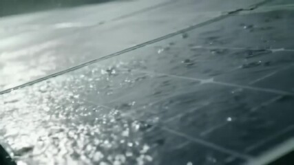 Observing rain falling on a textured surface, showcasing water droplets and reflecting the subdued, diffused light illuminating the damp, patterned texture. The  shot emphasizes the wetness.