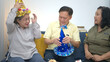 © Wosunan - Happy elderly man blowing out birthday candles surrounded by friends