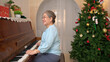 © Wosunan - On a holiday, an elderly woman enjoys decoration Christmas tree and playing the piano at home