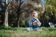 © qunica.com - A cute baby sits on green grass in a park under natural light. The background shows soft focus trees and surroundings, conveying a peaceful outdoor environment with vibrant and serene vibes.