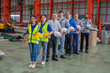 © reewungjunerr - Diverse team of engineers and factory workers standing in line inside an industrial warehouse, wearing safety gear and holding helmets, symbolizing teamwork and workplace diversity.