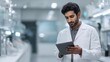 © Yuliia Malovana - Young scientist in a white lab coat using a digital tablet, monitoring scientific data and researching medical solutions in laboratory environment. Indian male doctor checks analysis results.