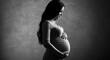 © albertART - A loving expectant mother tenderly caresses her pregnant belly in an artistic black and white studio portrait