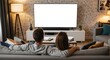© Elitemedia - A young couple sits together on a comfortable couch in their modern living room, watching a large television with a blank white screen perfect for mockups