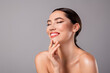 © Beauty Hero - Close up of a young brunette woman with radiant skin and a cheerful smile on a grey backdrop
