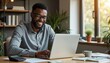 © Viktor - Smiling african man uses laptop at desk. He works in home office with calculator and cup of coffee. Successful black freelancer, entrepreneur. Happy person doing online work