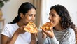 © Rich Ryns - Two friends with curly brown hair smile while eating a delicious slice of pizza , Two female friends cheerfully enjoy their pepperoni pizza while sitting on the couch in their living room