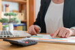 © Nanci - Businesswoman pointing at a printed chart on a desk, analyzing financial data and metrics with a laptop and calculator, planning strategy for growth and revenue