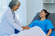 © ArLawKa - Elderly female doctor and Asian female patient are discussing something while sitting on hospital bed. Medical consultation concept.