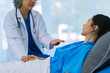 © ArLawKa - Elderly female doctor and Asian female patient are discussing something while sitting on hospital bed. Medical consultation concept.
