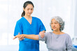 © ArLawKa - Young nurse trains elderly woman to exercise her arm during therapy and rehabilitation in her living room at home. Physical therapist.