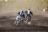 Rear view two motocross riders on track, clods earth from under rear wheels