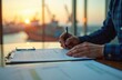 © miss irine - Man signs contract by office window overlooking harbor with ships. Golden sunset light illuminates desk with papers and pen. Professional worker focuses on paperwork, completing deal.