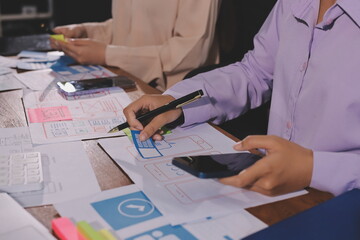Close up ux developer and ui designer brainstorming about mobile app interface wireframe design on table with customer breif and color code at modern office.Creative digital development agency.