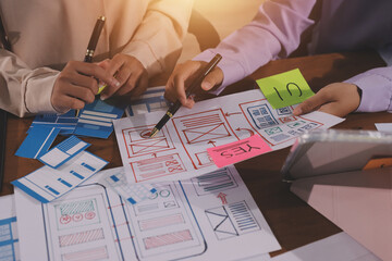Close up ux developer and ui designer brainstorming about mobile app interface wireframe design on table with customer breif and color code at modern office.Creative digital development agency.