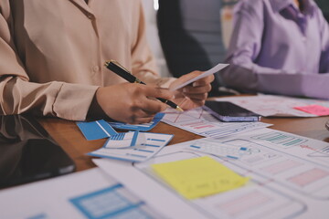 Close up ux developer and ui designer brainstorming about mobile app interface wireframe design on table with customer breif and color code at modern office.Creative digital development agency.