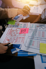 Close up ux developer and ui designer brainstorming about mobile app interface wireframe design on table with customer breif and color code at modern office.Creative digital development agency.