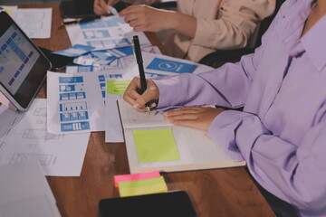 Close up ux developer and ui designer brainstorming about mobile app interface wireframe design on table with customer breif and color code at modern office.Creative digital development agency.