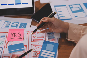 Close up ux developer and ui designer brainstorming about mobile app interface wireframe design on table with customer breif and color code at modern office.Creative digital development agency.