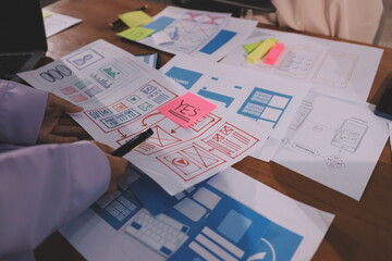 Close up ux developer and ui designer brainstorming about mobile app interface wireframe design on table with customer breif and color code at modern office.Creative digital development agency.