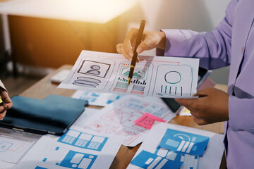 Close up ux developer and ui designer brainstorming about mobile app interface wireframe design on table with customer breif and color code at modern office.Creative digital development agency.